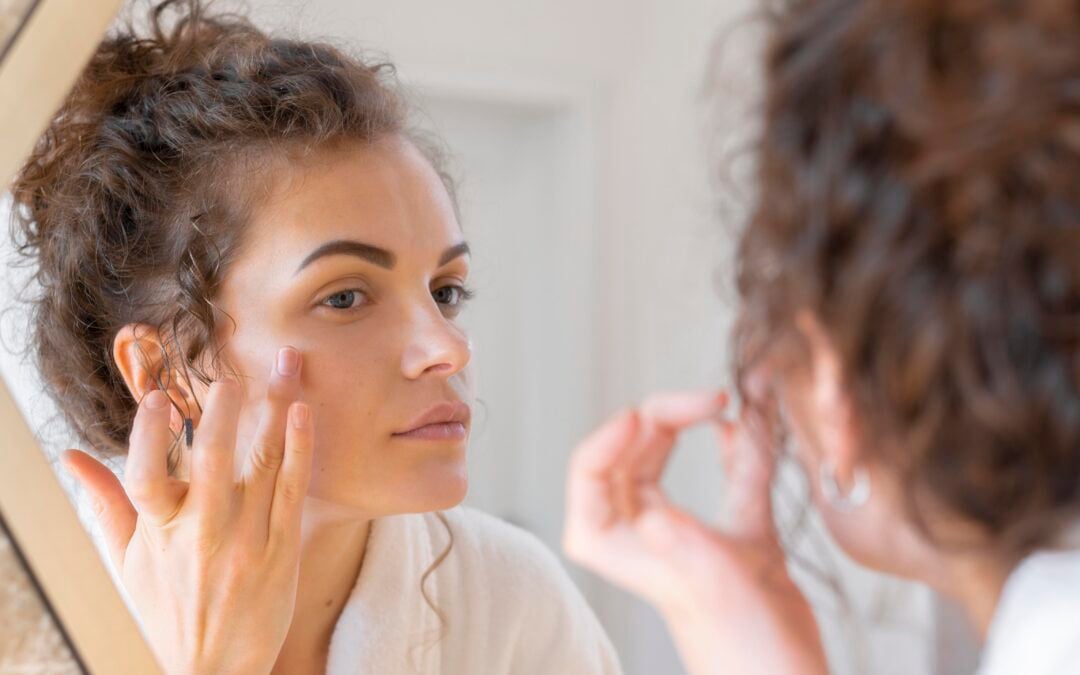 Mujer observando su piel frente al espejo como parte de su rutina de cuidado facial